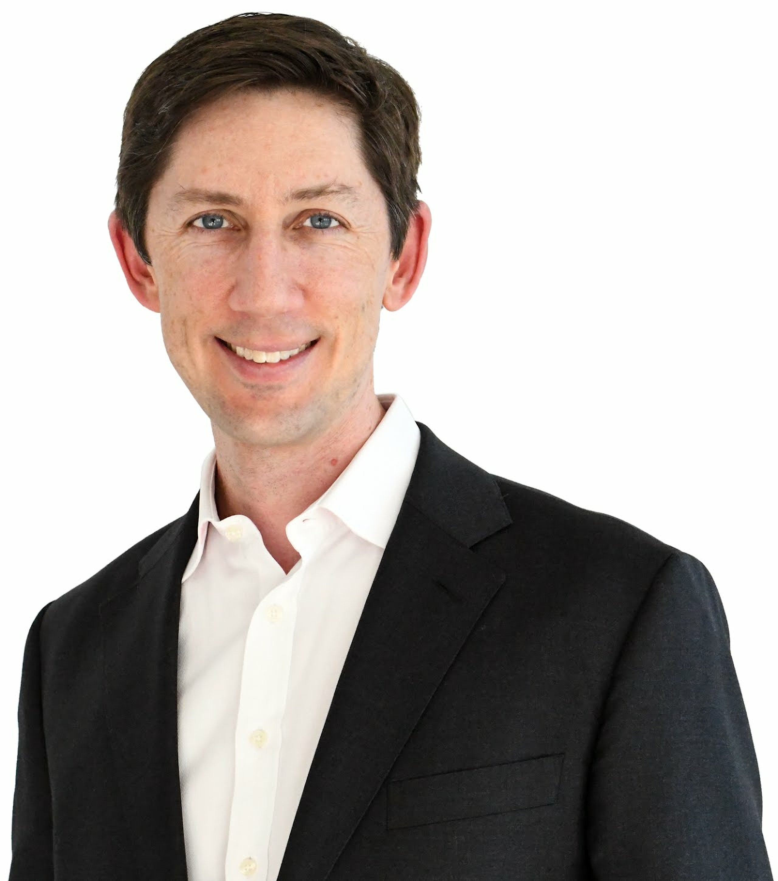 A professional headshot of a smiling man with brown hair and blue eyes, wearing a white shirt and a dark blazer against a plain white background.